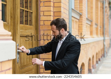 Businessman opening the large wooden door of a commercial brick building as he tries to enter the premises