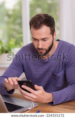 Man reading a message on his smartphone with a serious expression as he sits at his desk in the office