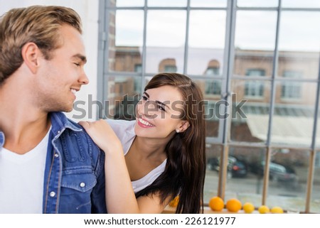 Happy affectionate young couple relaxing in the kitchen looking loving into each others eyes with an urban street visible through the window