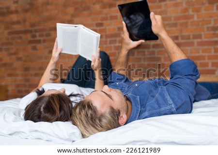 Couples Lying on White Bed while Girlfriend Reading a Book and Boyfriend Using Tablet.