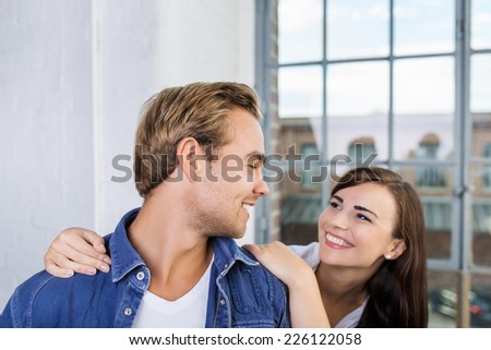 Playful loving couple standing in front of a large glass window smiling into each others eyes as the woman caresses her husbands shoulders