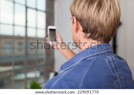 Over the shoulder view of a young blond man taking a selfie on his mobile phone posing for the camera