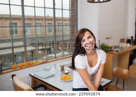 Pretty Smiling Young Woman in White Shirt Leaning on the Dining Table at Kitchen Area. Looking at the Camera.