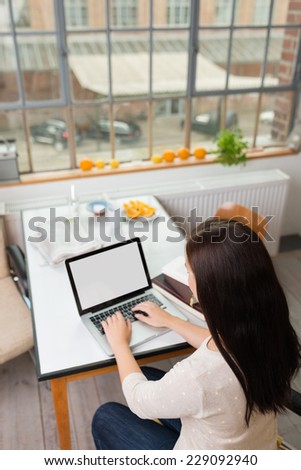 View from above of a young student working on a laptop at home sitting at the kitchen counter, view of the blank screen