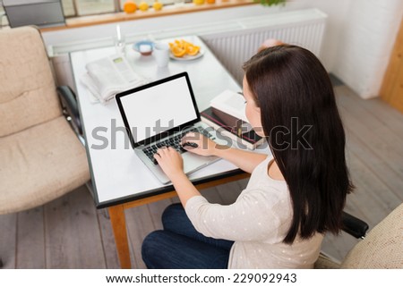 High angle view of a young woman working on a laptop computer at home in the kitchen, view of the blank screen