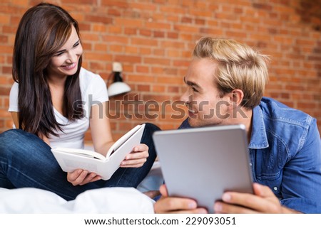 Close up Happy Young Lovers on Bed Facing Each Other While Holding Book and Tablet.