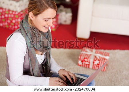 Happy Pretty Blond Woman with Neck Scarf Sitting on the Floor While Chatting Online Friends Using Laptop Computer Near Christmas Gift Box