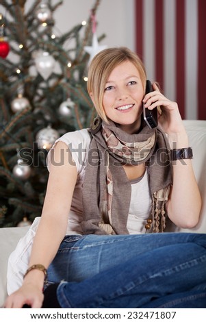 Young woman chatting to friends at Christmas on her mobile phone relaxing on a sofa in front of the Christmas tree