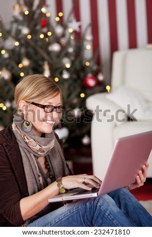 Sitting Happy Young Woman with Laptop Chatting with her Friends Through Internet on Christmas. Captured with Christmas Tree Decoration at the Background.