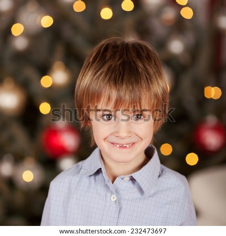Happy little boy standing in front of the lighted Christmas tree smiling at the camera with a cute gap toothed smile