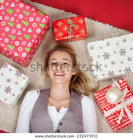 Happy woman lying on the floor, on a white carpet, surrounded by many gift boxes, wrapped in paper with Christmas pattern, high-angle