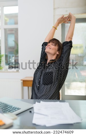 Young businesswoman stretching as she takes a break sitting back in her chair at the office with her hands raised and eyes closed in pleasure