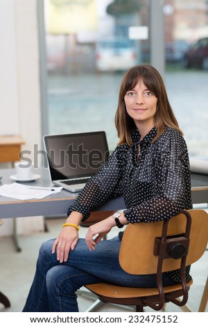 Stylish woman sitting at her desk in the office with a laptop computer and coffee smiling at the camera