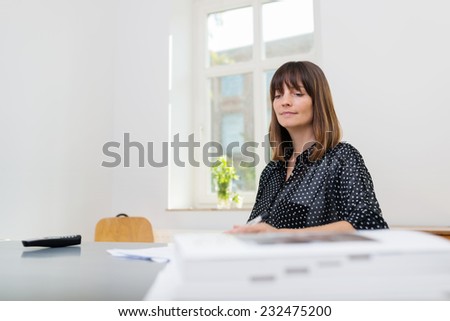 Low angle view across the surface of her desk of a young businesswoman working in the office