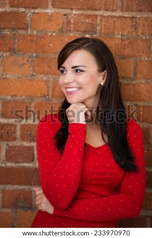 Close up Attractive Young Woman in Casual Red Long Sleeve Shirt Facing Right with Hand Below the Chin. Captured on a Brick Wall Background.