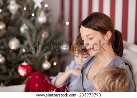 Young family waiting for Father Christmas or Santa Claus sitting on a couch alongside the decorated tree reading a book