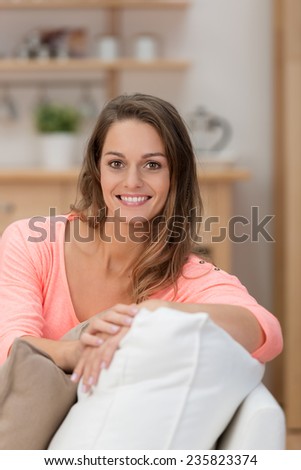 Confident friendly young woman relaxing at home sitting on a comfortable sofa looking at the camera with a lovely warm smile