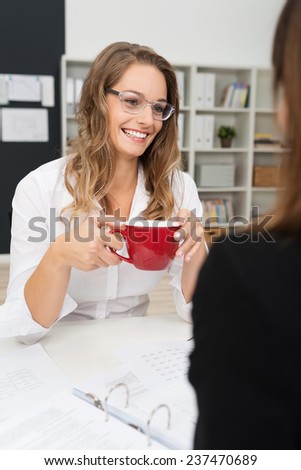 Happy White Office Girl Wearing Long Sleeve Shirt and Eyeglasses, Having Coffee Break with Co-worker at her Worktable.