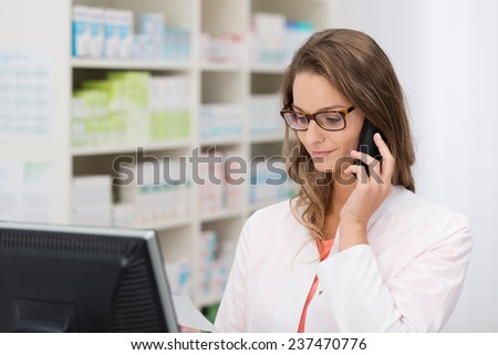 Smiling female pharmacist taking call on her mobile phone as she discusses a prescription with a patient