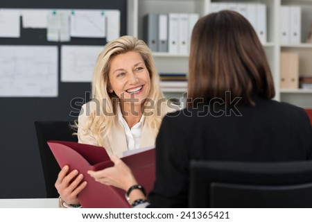 Attractive manageress conducting a job interview with a female applicant smiling at her as they discuss her CV