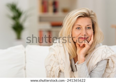 Attractive middle-aged woman sitting on a sofa at home daydreaming resting her chin on her hand staring to the side with a dreamy thoughtful expression