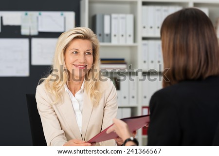 View from behind of a female job applicant handing over her CV to a smiling middle-aged manageress