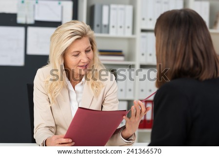 Female personnel officer doing a job interview with a female applicant reading through a file containing her CV