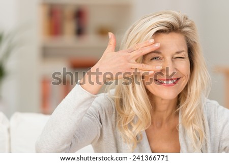 Fun woman peering between her fingers at the camera with a playful smile as she relaxes at home in the living room