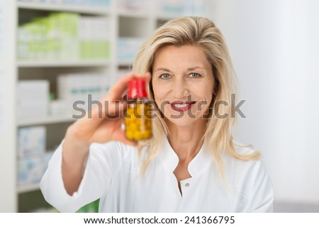 Smiling attractive middle-aged lady pharmacist holding a bottle of tablets in her hand with focus to her face