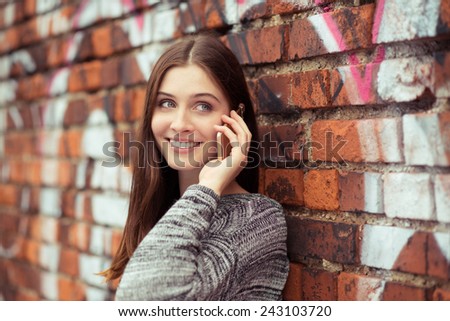 Close up Attractive Young Woman with Long Brown Hair Talking to Someone Through Cellphone While Leaning on Brick Wall at the Street.