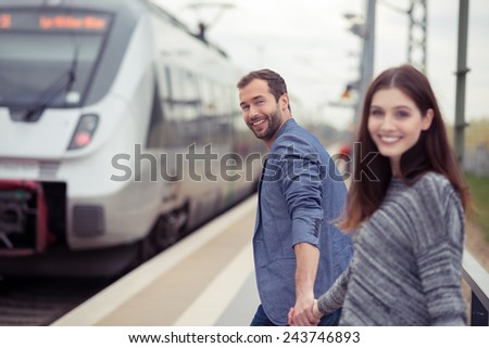 Young couple about to board a train at the station holding hands as they laugh and smile at the camera