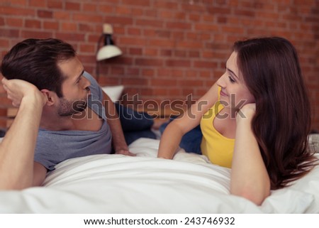 Romantic couple relaxing together on the bed lying propped up on one elbow looking lovingly into each others eyes