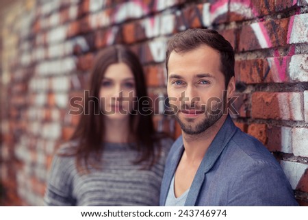 Handsome young man smiling at the camera as he stands against a brick wall with graffiti alongside his girlfriend