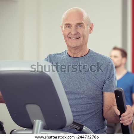 Athletic senior man working out a gym on the exercise equipment looking at the camera with a friendly happy smile