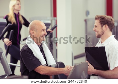 Happy attractive elderly man shaking hands with a trainer at the gym as he does his weekly exercises in a healthy and fitness concept