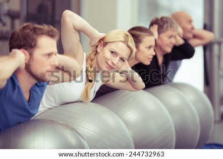Pilates class at a gym with diverse people in a receding row exercising with their gym balls, young and elderly, men and women, with focus to an attractive blond woman