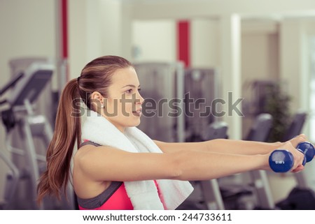 Head and shoulders profile view of an athletic attractive young woman working out with dumbbells in a gym in a health and fitness concept