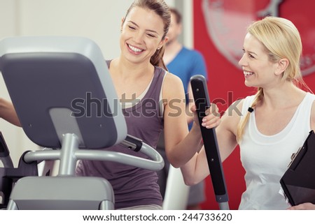 Two young woman enjoying their exercise routine at the gym laughing and smiling as they watch the digital readout on the machine in a healthy lifestyle concept