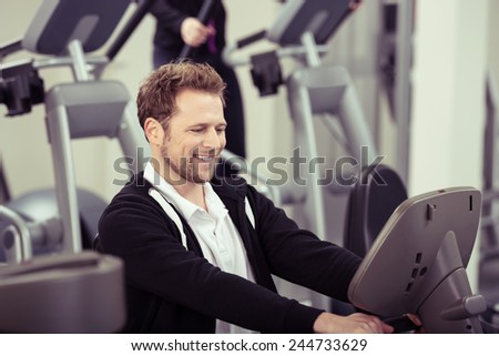 Enthusiastic young man working out in a gym smiling happily as he watches the digital readout on the monitor showing his performance