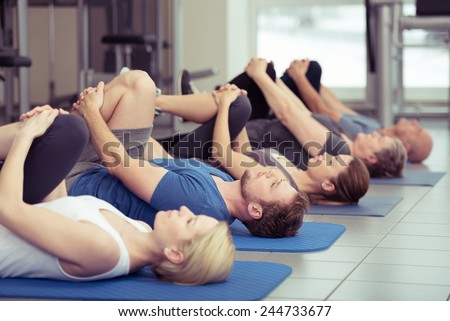 Diverse group of people in a gym class lying in a receding row on mats doing leg flexes in a health and fitness concept