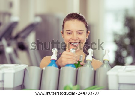 Young woman pouring isotonic energy drink from a dispenser in a gym to rehydrate after a workout in a health and fitness concept