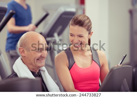 Young physical trainer with a smiling happy fit senior man in the gym discussing his exercise regime and training