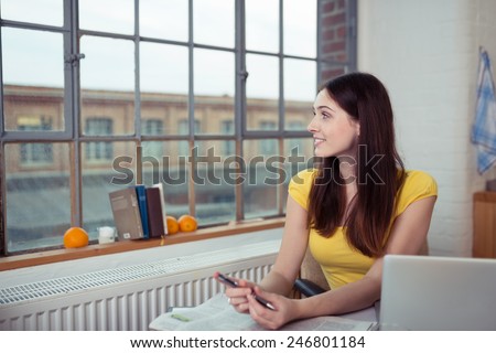 Young woman sitting staring out of a window in her apartment at the street outside with a smile on her face