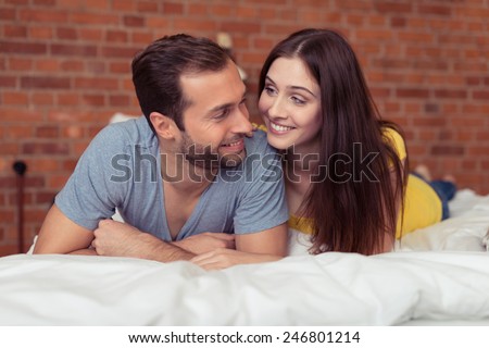 Young couple spending a lazy day relaxing at home lying on the bed smiling affectionately at each other