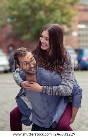Playful attractive affectionate young couple enjoying a piggy back ride in an urban street smiling and laughing together