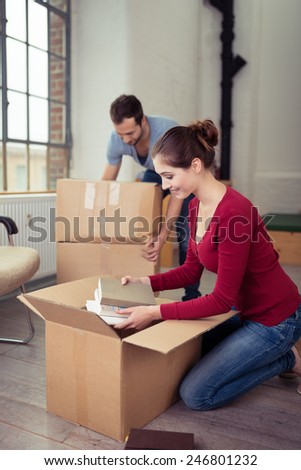 Young couple moving house busy in the living room packing or unpacking cardboard boxes with books and personal possessions
