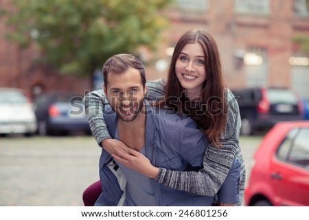 Happy couple enjoying a fun piggy back ride in an urban street looking at the camera with carefree friendly smiles