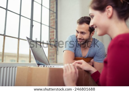 Young Happy White Partners Browsing Internet Using Laptop Computer on the Table Near Glass Windows Inside the House.