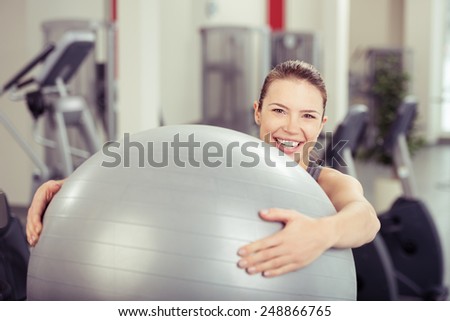 Young woman doing pilates exercises at the gym holding the gym ball in her arms and smiling over the top at the camera in a health and fitness concept
