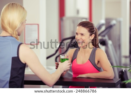 Young woman getting a high energy drink at the gym smiling as the girl behind the bar hands over the glass of refreshment after a workout
